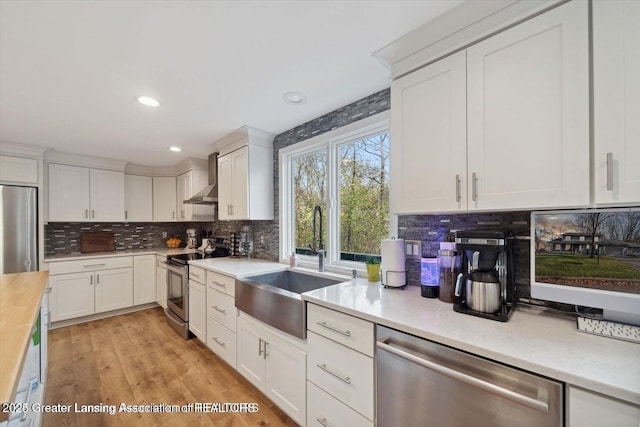 kitchen with wall chimney exhaust hood, sink, tasteful backsplash, appliances with stainless steel finishes, and white cabinets