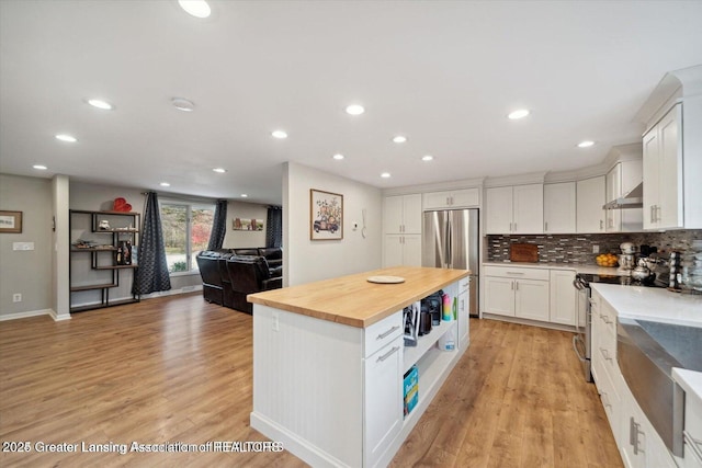 kitchen featuring appliances with stainless steel finishes, butcher block counters, white cabinetry, a center island, and light hardwood / wood-style floors