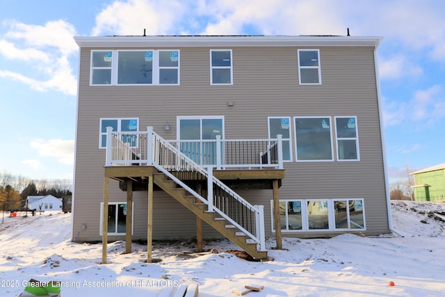 snow covered rear of property with a deck and stairway