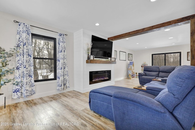 living room featuring a large fireplace, beam ceiling, and light hardwood / wood-style flooring