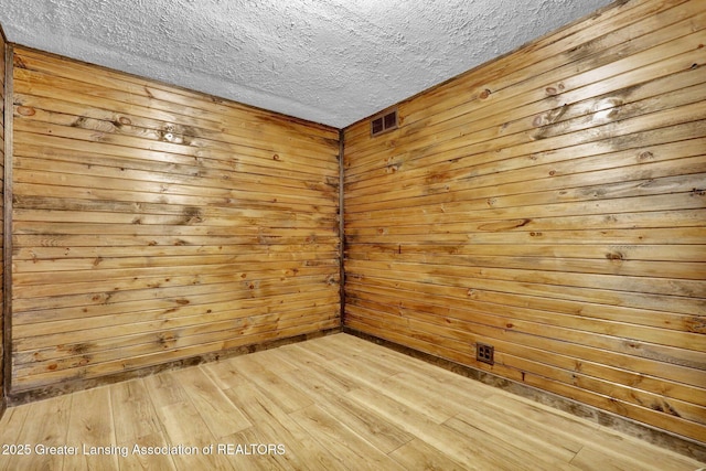 empty room with wooden walls, a textured ceiling, and light hardwood / wood-style flooring