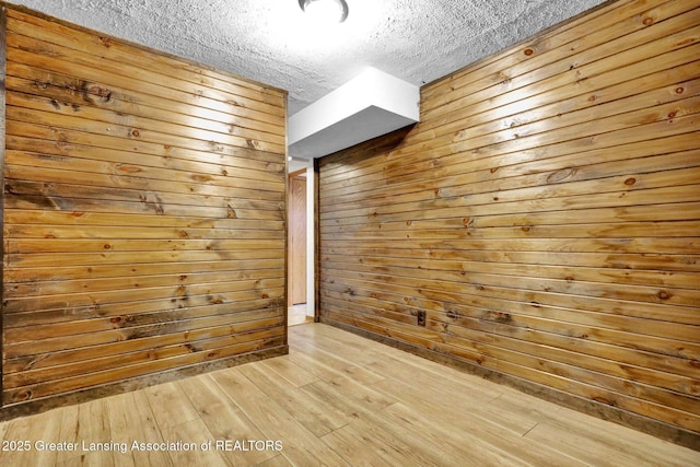 unfurnished room featuring light wood-type flooring, a textured ceiling, and wood walls