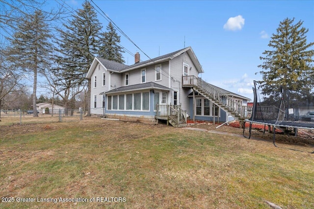 rear view of house with a trampoline, a chimney, fence, and a lawn