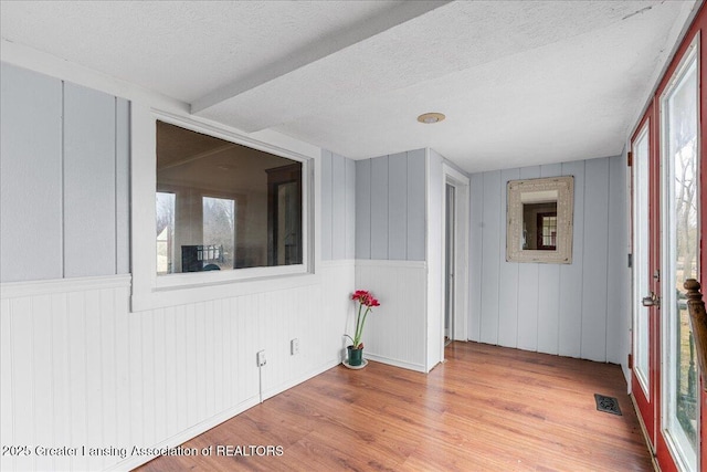 spare room with a healthy amount of sunlight, a textured ceiling, visible vents, and wood finished floors