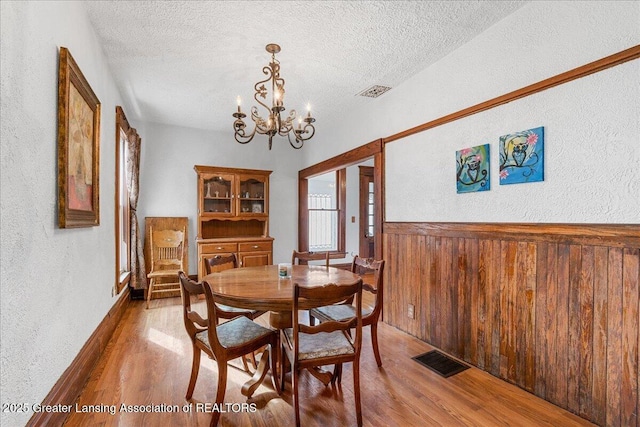 dining area with a wainscoted wall, visible vents, wood walls, a textured ceiling, and wood finished floors