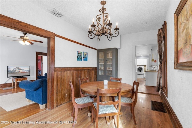 dining space with a textured ceiling, a wainscoted wall, visible vents, light wood-type flooring, and washer / dryer