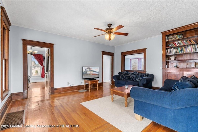 living area with light wood-type flooring, a ceiling fan, baseboards, and a textured ceiling