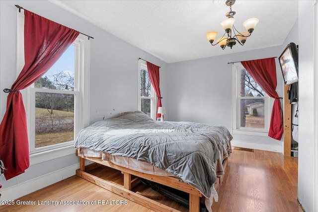 bedroom with a notable chandelier, a textured ceiling, baseboards, and wood finished floors