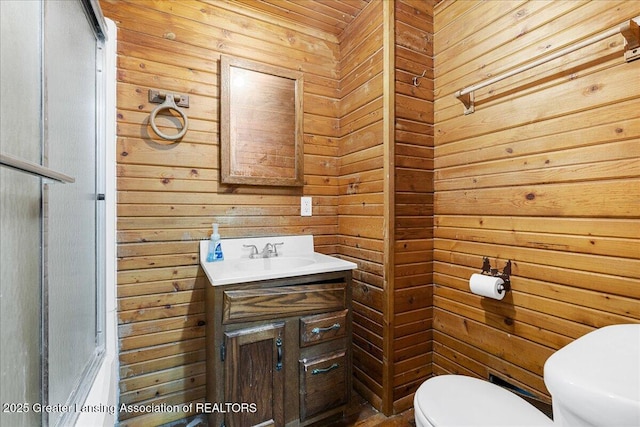 full bath with wood walls, vanity, toilet, and a shower with door