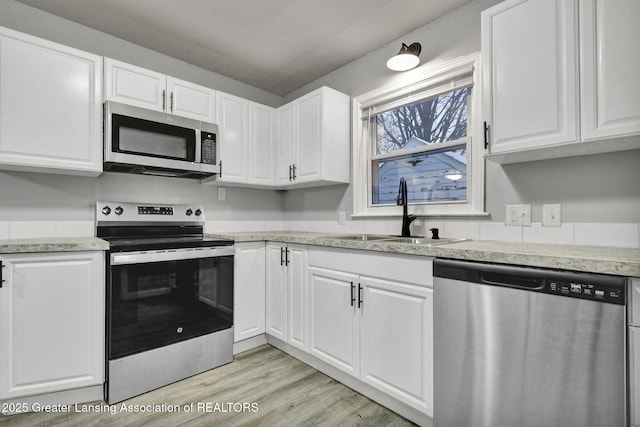 kitchen with white cabinetry, appliances with stainless steel finishes, sink, and light hardwood / wood-style flooring