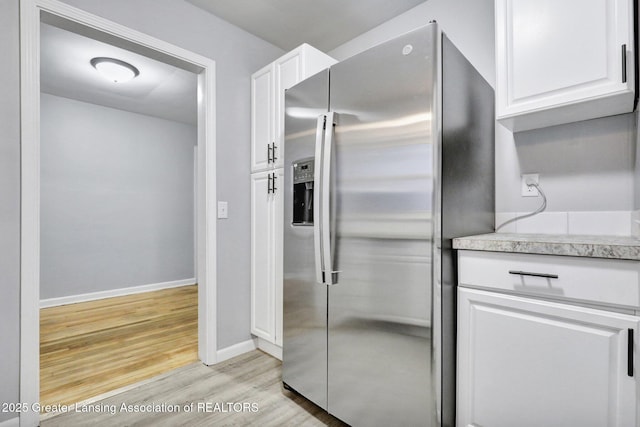 kitchen with stainless steel refrigerator with ice dispenser, white cabinetry, and light hardwood / wood-style floors