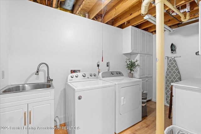 clothes washing area with cabinets, sink, washer and clothes dryer, and light hardwood / wood-style floors