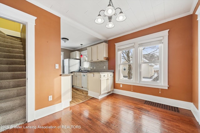 kitchen featuring crown molding, white appliances, light hardwood / wood-style flooring, hanging light fixtures, and backsplash