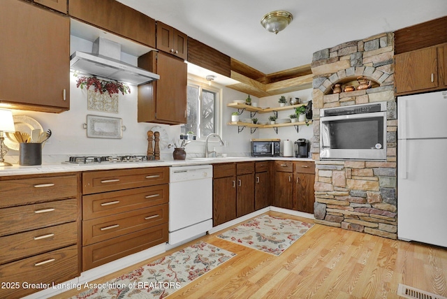 kitchen featuring light wood-type flooring, appliances with stainless steel finishes, sink, and wall chimney range hood