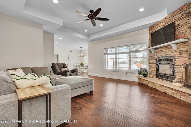 living room featuring a raised ceiling, ceiling fan, a stone fireplace, and dark hardwood / wood-style flooring