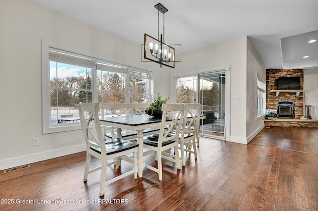 dining space featuring a stone fireplace, dark hardwood / wood-style floors, and a chandelier