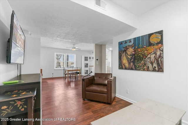 sitting room with ceiling fan, dark wood-type flooring, and a textured ceiling