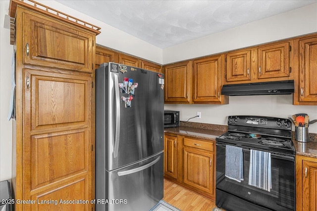 kitchen with dark stone countertops, stainless steel fridge, electric range, and light hardwood / wood-style flooring