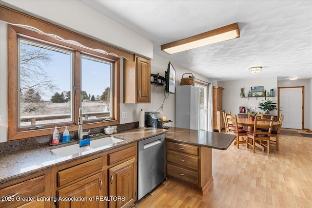 kitchen with sink, light wood-type flooring, stainless steel dishwasher, kitchen peninsula, and dark stone counters