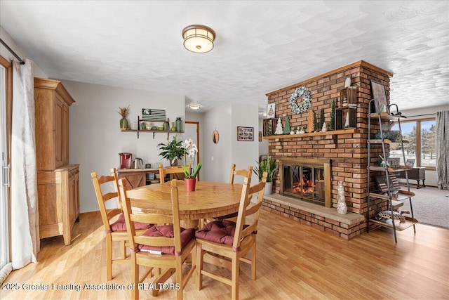 dining space with light hardwood / wood-style floors, a brick fireplace, and a textured ceiling