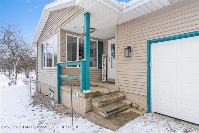 snow covered property entrance featuring a garage