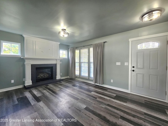 unfurnished living room featuring a brick fireplace, plenty of natural light, and dark wood-type flooring