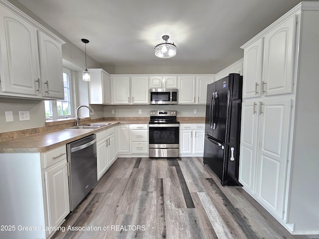 kitchen featuring appliances with stainless steel finishes, pendant lighting, sink, white cabinets, and light hardwood / wood-style flooring