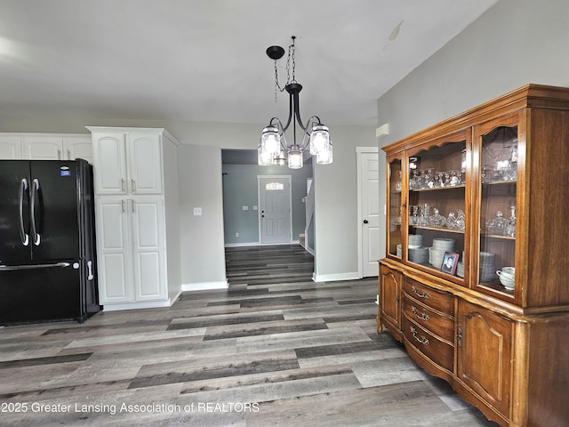 interior space with pendant lighting, white cabinets, dark hardwood / wood-style flooring, black fridge, and an inviting chandelier