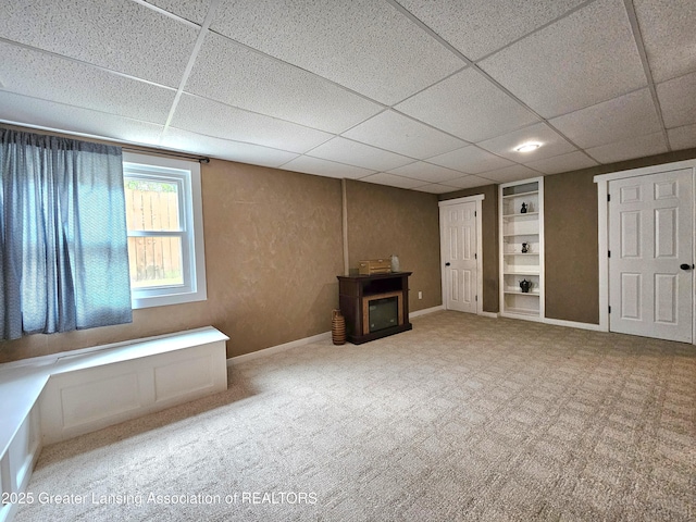 basement with carpet floors, built in features, and a paneled ceiling