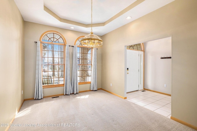 empty room with a raised ceiling, carpet flooring, visible vents, and a healthy amount of sunlight