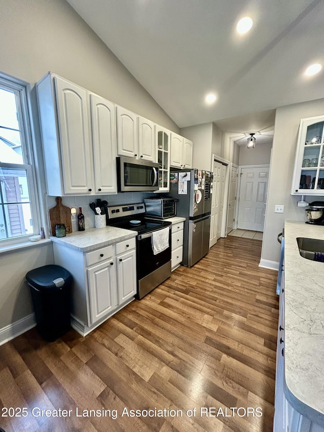 kitchen with lofted ceiling, sink, white cabinetry, appliances with stainless steel finishes, and hardwood / wood-style flooring