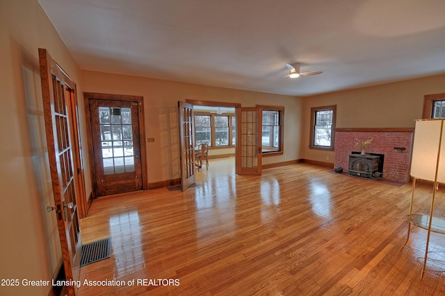 unfurnished living room with light wood-type flooring, french doors, a wood stove, and ceiling fan