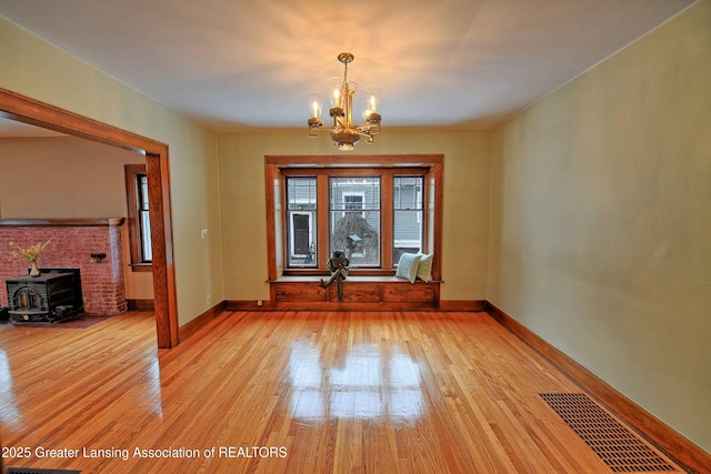 unfurnished dining area with light wood-type flooring, a wood stove, and a chandelier