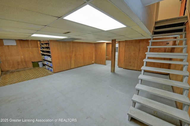 basement with a drop ceiling and wooden walls