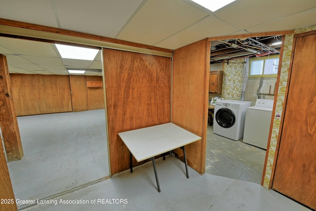 basement featuring washing machine and dryer, a paneled ceiling, and wood walls