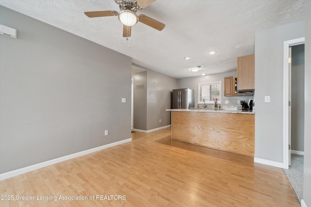 kitchen with light hardwood / wood-style flooring, stainless steel fridge, a textured ceiling, and kitchen peninsula