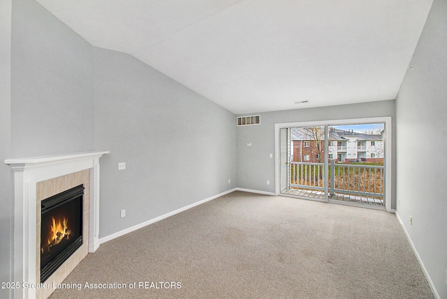 unfurnished living room with a tiled fireplace, lofted ceiling, and carpet flooring