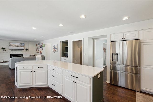 kitchen featuring a kitchen island, white cabinets, stainless steel fridge with ice dispenser, and a brick fireplace