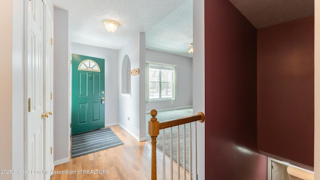 entryway with a ceiling fan, light wood-style flooring, baseboards, and a textured ceiling