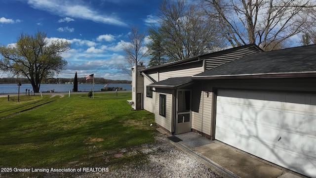 view of side of property featuring an attached garage, a water view, a chimney, a lawn, and roof with shingles