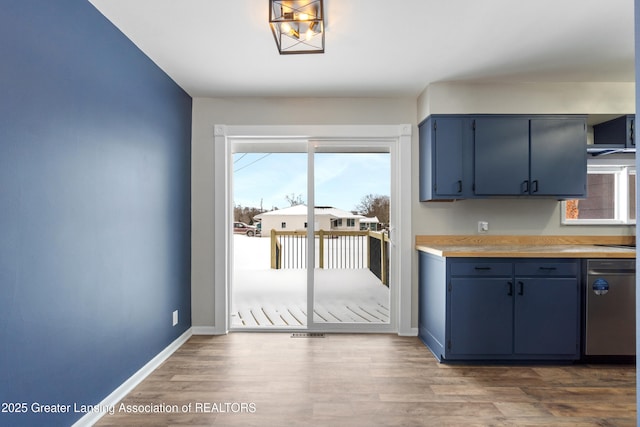 kitchen featuring blue cabinets, wood finished floors, baseboards, light countertops, and stainless steel dishwasher