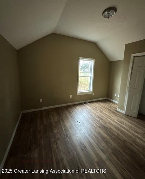 additional living space with visible vents, baseboards, vaulted ceiling, and wood finished floors