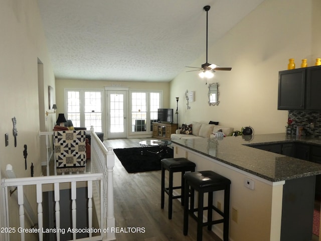 kitchen featuring a peninsula, open floor plan, vaulted ceiling, dark stone counters, and a kitchen bar