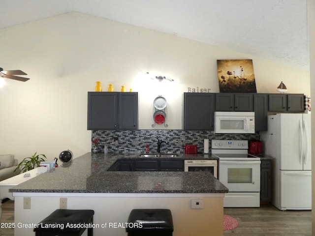 kitchen featuring a peninsula, white appliances, a sink, vaulted ceiling, and a kitchen bar