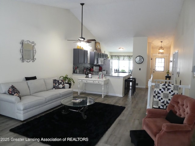 living room with high vaulted ceiling, a ceiling fan, baseboards, and wood finished floors