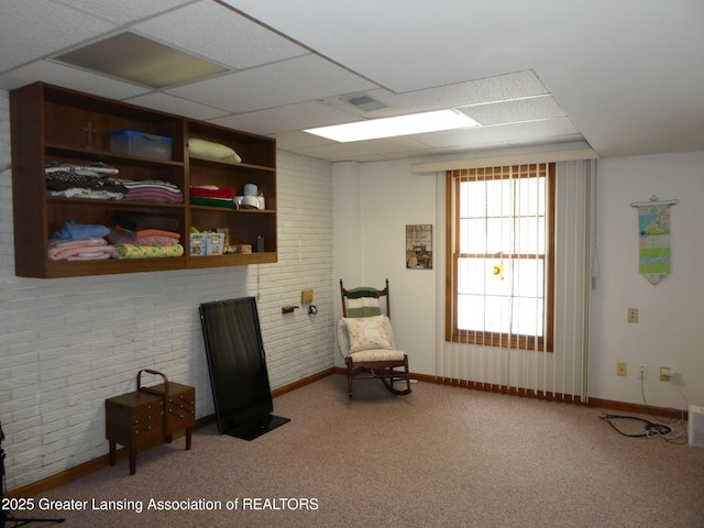 living area featuring brick wall, carpet flooring, a paneled ceiling, and baseboards