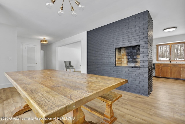 dining space featuring light wood finished floors, brick wall, and baseboards