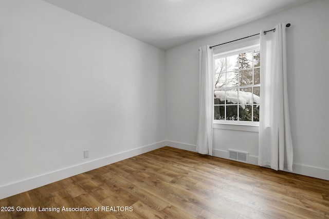 empty room featuring light wood-style flooring, visible vents, and baseboards