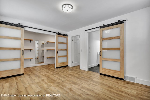 unfurnished bedroom featuring light wood finished floors, a barn door, visible vents, and baseboards