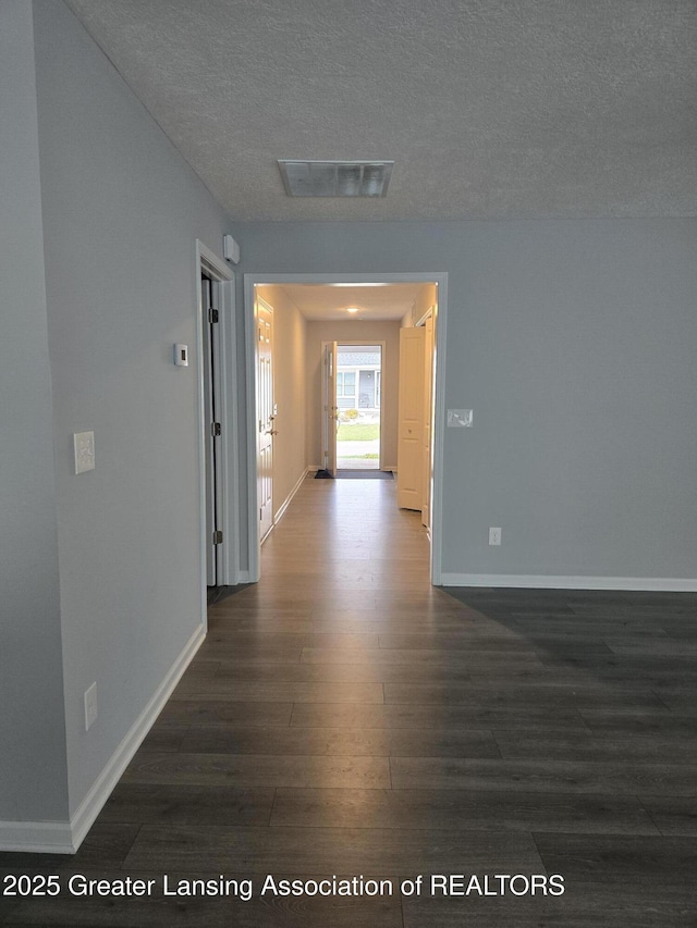 corridor featuring baseboards, a textured ceiling, visible vents, and dark wood-type flooring